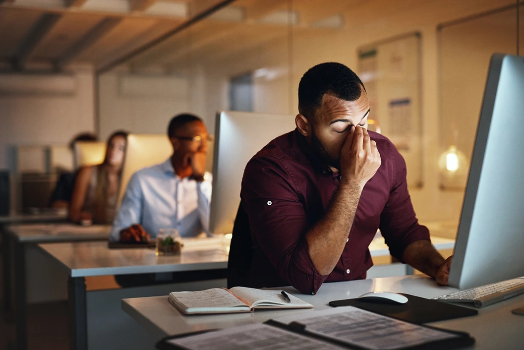 View of four people working in an office. One man is pinching the top of his nose, indicating he's stressed.