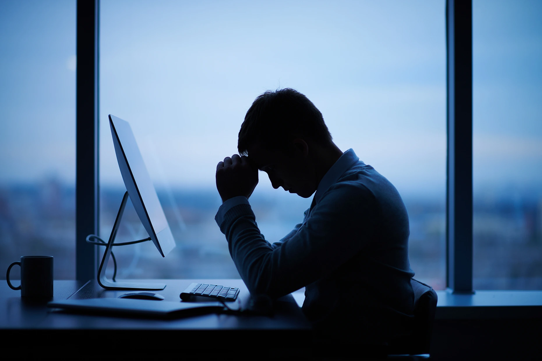 Side view of a man sitting at his desk with his fist to his head.